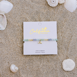 Bracelet on a 'California' branded card with seashells around on sand