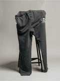 A pair of men's joggers with drawstrings, featuring a large front pocket and a smaller back pocket, and a decorative skull and crossbones emblem on the left thigh.