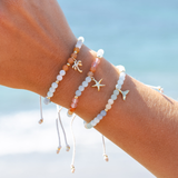 Bracelets with various charms on a wrist against a beach background