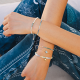 Close-up of a person's wrist wearing multiple bracelets on a blue patterned fabric background