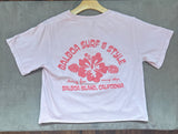 A light pink short-sleeve t-shirt with a magenta graphic print reading 'BALBOA SURF & STYLE' and 'BALBOA ISLAND, CALIFORNIA' around a hibiscus flower, 