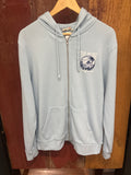 A light blue zip-up hoodie with drawstring hood, and a circular chest graphic.