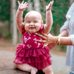 Baby in a pink dress with ruffles standing on a wooden log outdoors