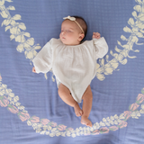 Newborn baby in a white outfit lying on a blue floral-patterned blanket