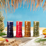 Four colorful tiki mugs on a tropical setting with a pineapple and lemon.
