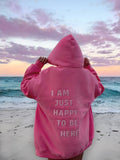 Person wearing a pink hoodie with a quote on a beach at sunset