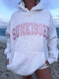 Person wearing a hoodie with 'SUNKISSED' text on a beach