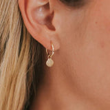Close-up of a gold hoop earring with a shell charm
