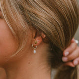 Close-up of a person wearing gold hoop earrings with a pearl drop and a gold seashell stud earring.