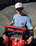 Man holding a red toolbox wearing a Volcom cap in an outdoor setting
