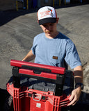 Man holding a red toolbox wearing a Volcom cap in an outdoor setting