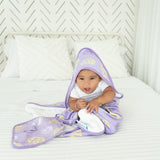 Baby sitting on a bed wearing a purple hooded towel with yellow patterns