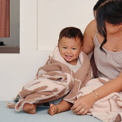 Child wrapped in a cozy brown blanket sitting next to an adult 