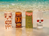 Four tiki-style ceramic vases on a beach with ocean in the background